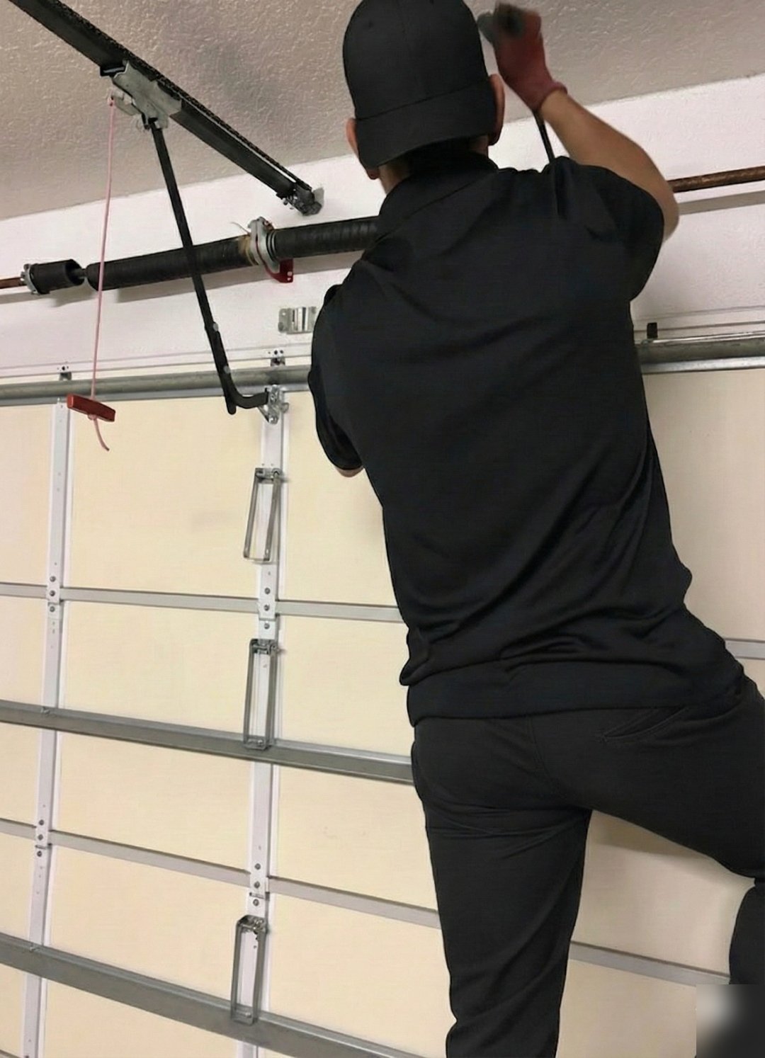 Worker reaching up to the opener rail above a closed white garage door
