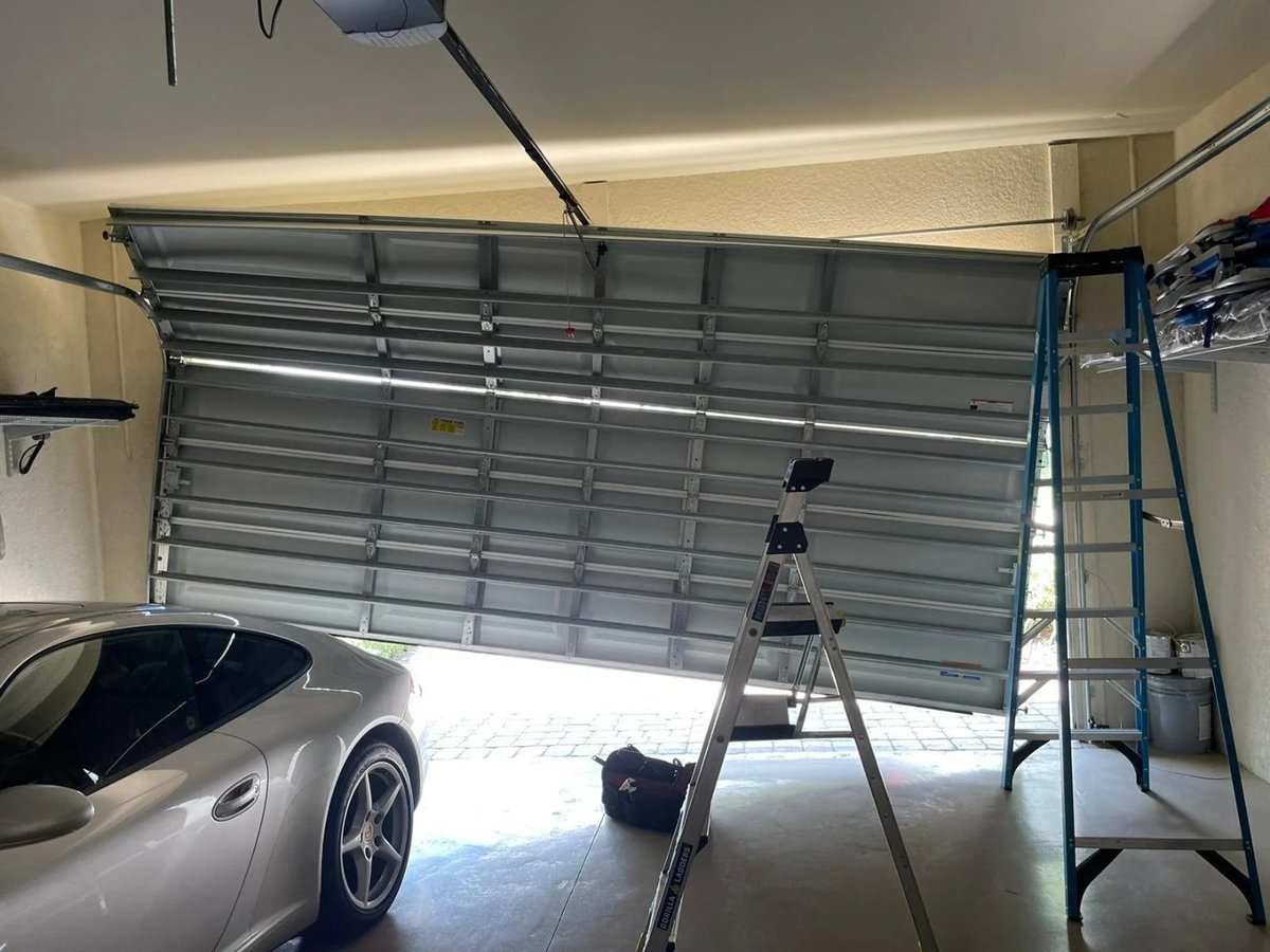 Step ladder below an open sectional door with a car parked to one side