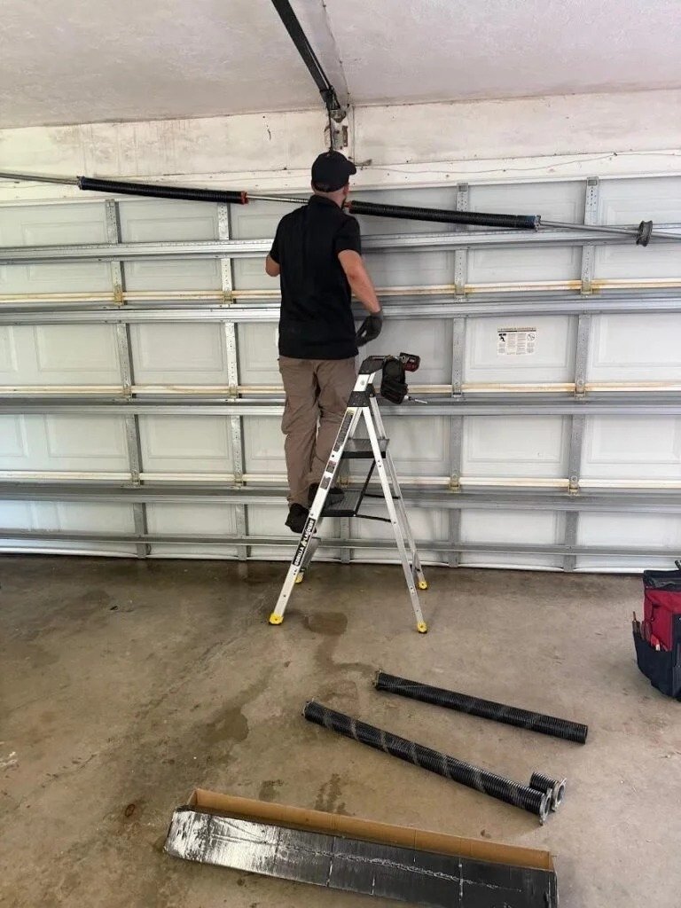 Technician on a stepladder at the spring shaft with removed parts lying on the floor