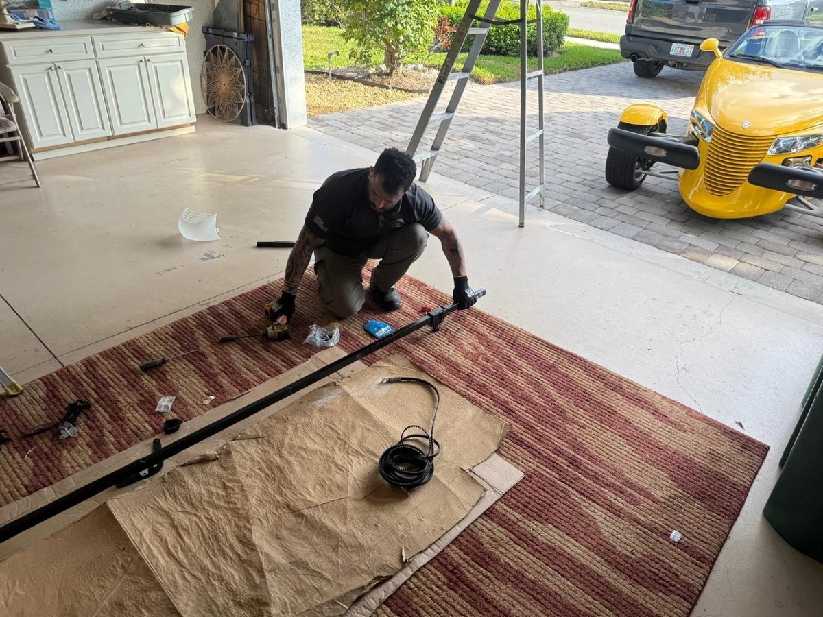 Technician kneeling on a garage floor working on a long steel track section
