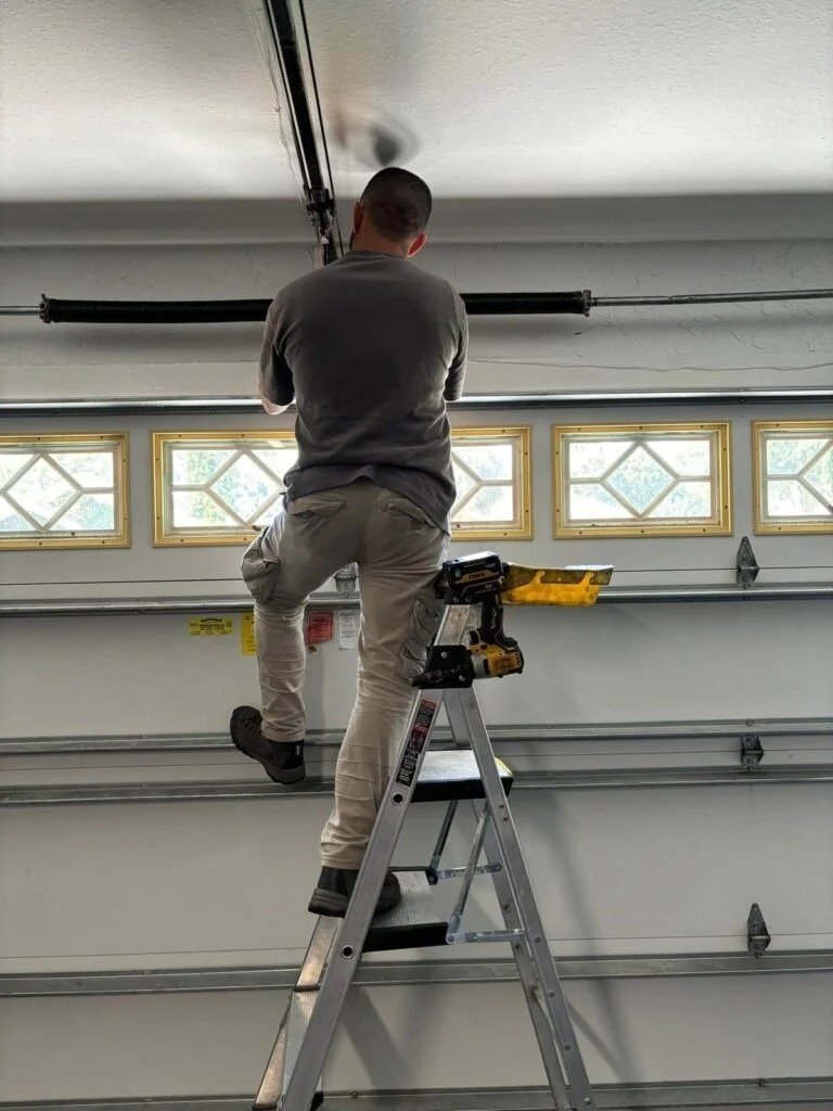 Technician on a stepladder checking hardware above a garage door with window panels