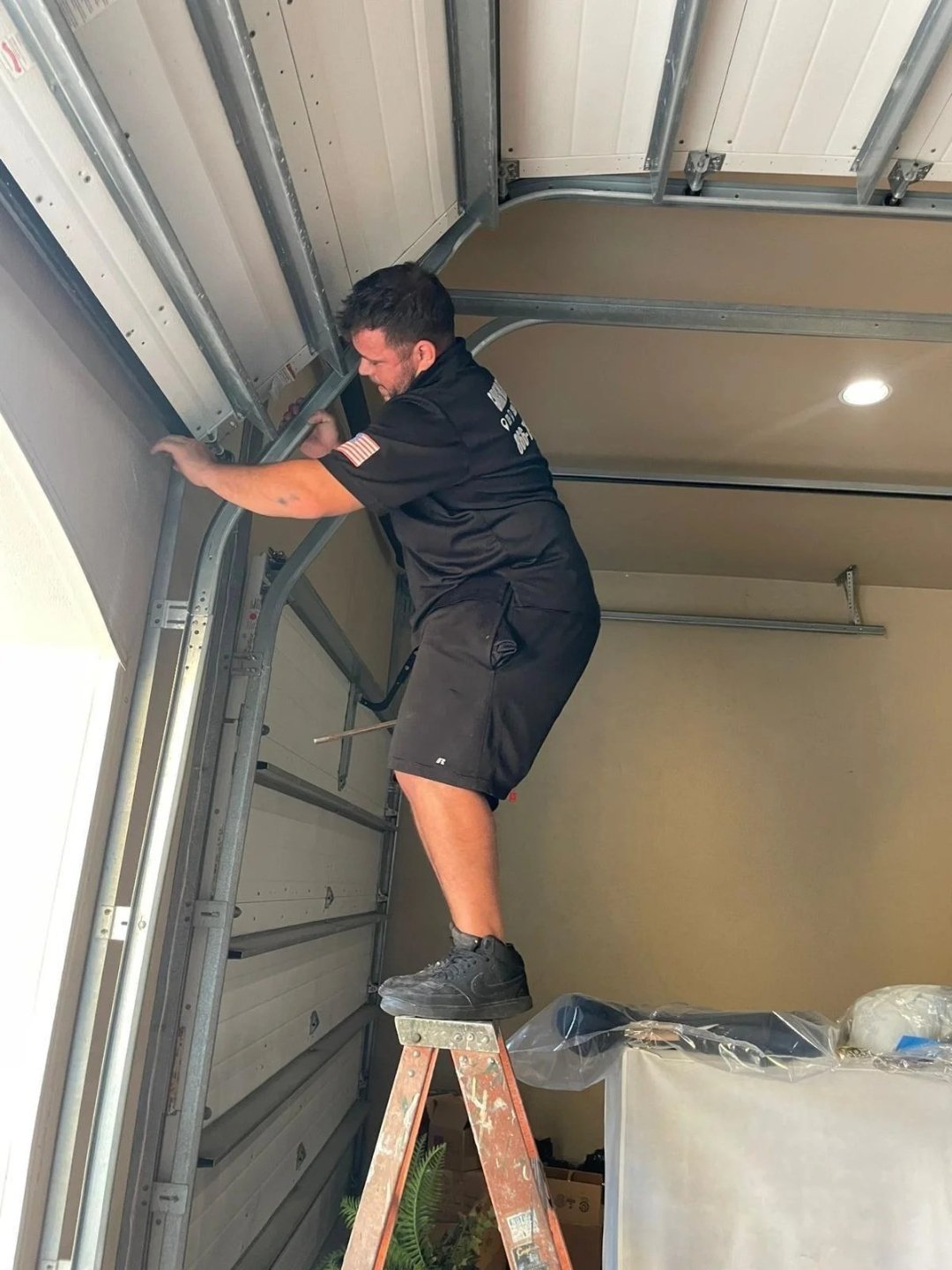Technician on a ladder reaching into the garage ceiling beside the door track