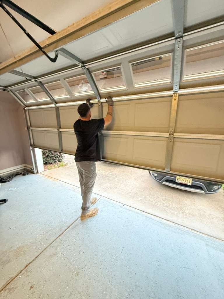 Technician standing under a raised sectional garage door, checking the top track